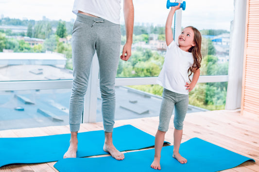 Man and young girl exercising with dumbbells on blue mats in a bright room with large windows.
